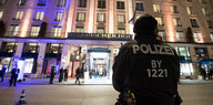 Ein Polizist steht vor dem in der Dunkelheit violett und gelb erleuchteten Hotel Bayerischer Hof in München
