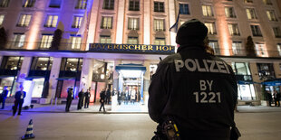 Ein Polizist steht vor dem in der Dunkelheit violett und gelb erleuchteten Hotel Bayerischer Hof in München