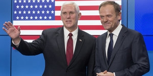 Zwei Männer in Anzügen stehen vor einer US-amerikanischen Flagge