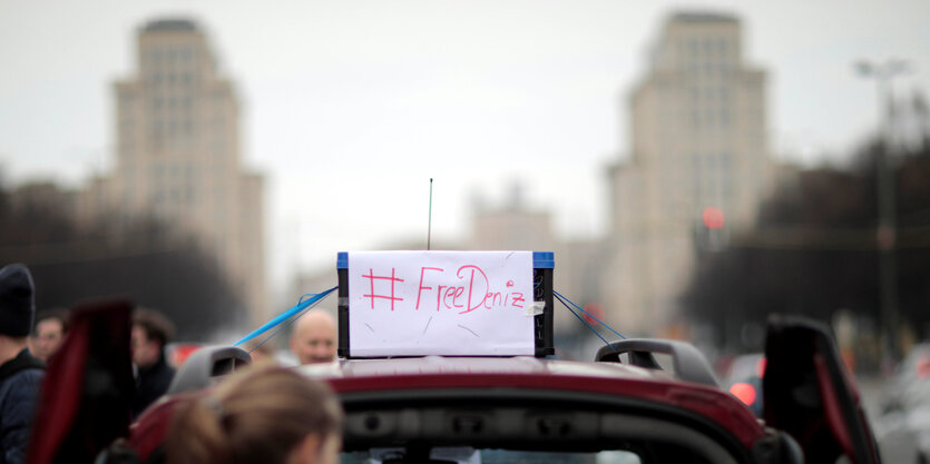 Auto mit Schild „Free Deniz“, dahinter Gebäude