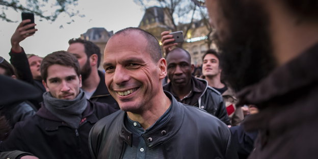 Yanis Varoufakis ist von Menschen umringt und grinst in die Kamera