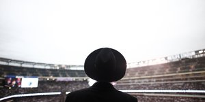Ein Mann mit Hut von hinten, er schaut in ein Stadionrund