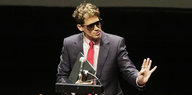 Ein Mann in Anzug und mit Sonnenbrille hält eine Rede an einem Rednerpult