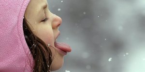 Ein Mädchen streckt die Zunge raus, um mit ihr Schneeflocken aufzufangen.