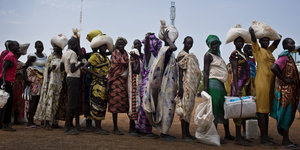Mehrere Frauen und Mädchen stehen in einer Schlange und tragen auf ihren Köpfen Pakete
