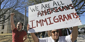 Eine Demonstrantin hält ein Schild hoch: "we are all immigrants" steht darauf, ein "Americans" ist durchgestrichen