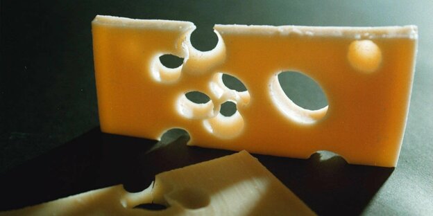 Eine Scheibe Schweizer Käse hochkant im Gegenlicht, davor liegt eine weitere Scheibe im Schatten