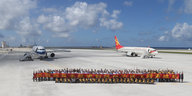 Eine Gruppe von Menschen post vor zwei zivilen Flugzeugen aus dem Fiery Cross Atoll