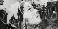 Schwarz-weiß-Aufnahme eines nach oben schauenden Frauengesichts im Profil, im Hintergrund schimmern Gebäude durch