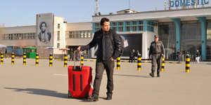 Ein Mann mit Rollkoffer vor dem Flughafen Kabul