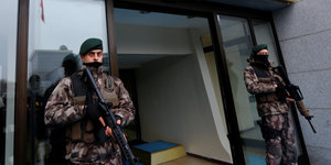 Zwei bewaffnete Männer stehen vor einem Hauseingang