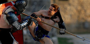 Darsteller in römischen Rüstungen stellen einen Gladiatorenkampf nach