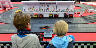 Kinder stehen an einer Spielzeug-Rennbahn