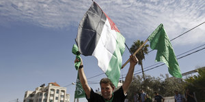 Ein Mann schwenkt die palästinensische und die islamische Flagge vor blauem Himmel
