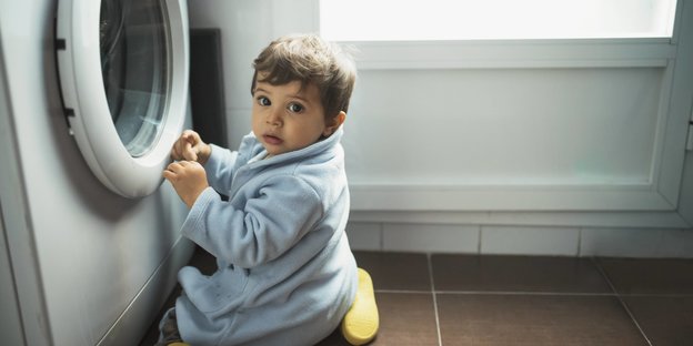 Ein kleines Kind sitzt staunend vor einer Waschmaschine