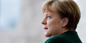 Angela Merkel steht im flaschengrünen Sakko allein und mit gefalteten Händen und guckt visionär