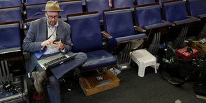 Ein Mann sitzt mit seinem Handy und Laptop in einer Stuhlreihe