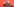 Ein junger Mann in einer olivgrünen Jacke posiert mit angewinkelten Armen und lacht vor einer hellroten Wand