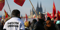 Im Hintergrund der Kölner Dom, im Vordergrund mehrere Demonstranten mit roten Flaggen