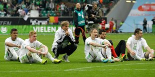 Mehrere Fußballleute sitzen auf dem Rasen und gucken nach vorne