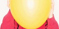 Jemand hält sich einen gelben Luftballon vor das Gesicht