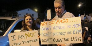 Eine Frau und ein Mann stehen beisammen und halten Protest-Plakate in die Kamera