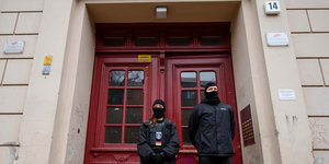 Zwei Personen mit Sturmhaube stehen vor einer roten Eingangstür