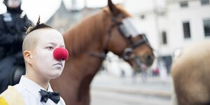 Foto, von einem Clown, der mit roter Nase vor einem Pferd steht