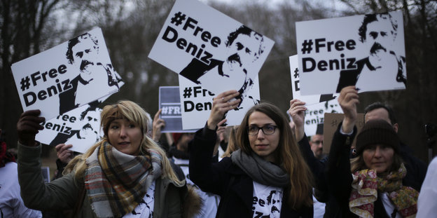 Drei Frauen führen eine Gruppe Protestierender an und halten „Free Deniz“-Schilder in die Luft