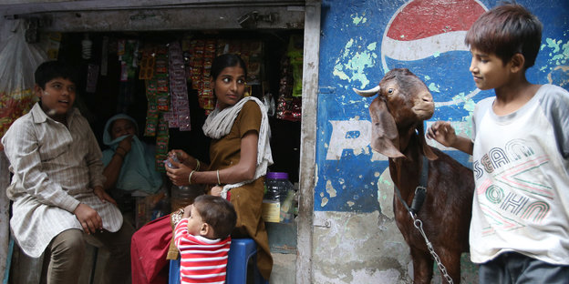 Menschen und eine Ziege vor einem kleinen Laden umrandet von Pepsi-Werbung