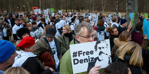 Viele Menschen stehen zusammen. Ein Mann hält ein Schild vor seine Nase. Darauf steht: Free Deniz