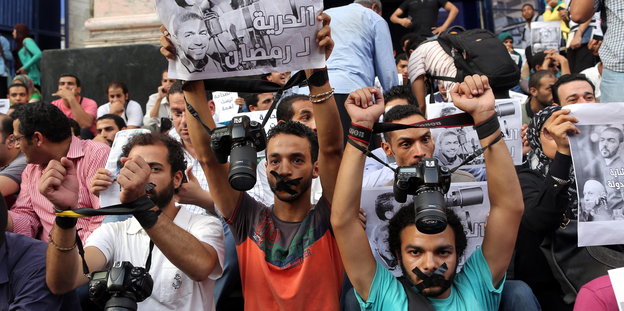 Journalisten haben sich die Münder verklebt und halten ihre Kameras in die Höhe