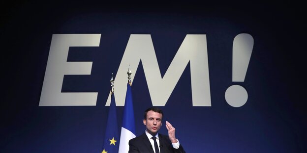 Macron auf einer Bühne vor seinen überdimensionierten Initialen „EM!“
