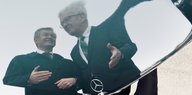 Die Reflektion von zwei Männern auf der Motorhaube eines Mercedes, dessen Stern man sieht