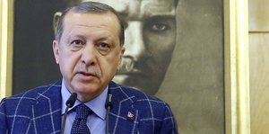 Ein Mann spricht in ein Mikrofon. Hinter ihm hängt ein Portrait des türkischen Staatsgründers Atatürk