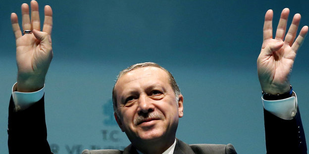 Erdoğan hebt beide Hände zum Gruß bei einer Rede.