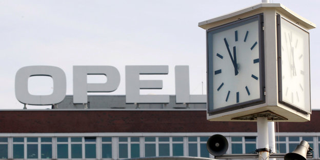 ein Opel-Logo im öffentlichen Raum, davor eine Uhr