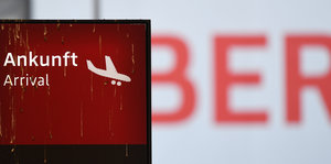 Eine rote Anzeigetafel zeigt ein landendes Flugzeug, daneben steht „Ankunft“ und „Arrival“