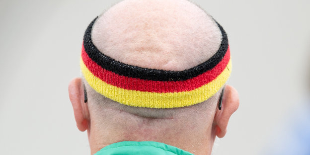 Ein alter Mensch mit wenigen Haaren auf dem Kopf, trägt ein Stirnband in schwarz-rot-gelb