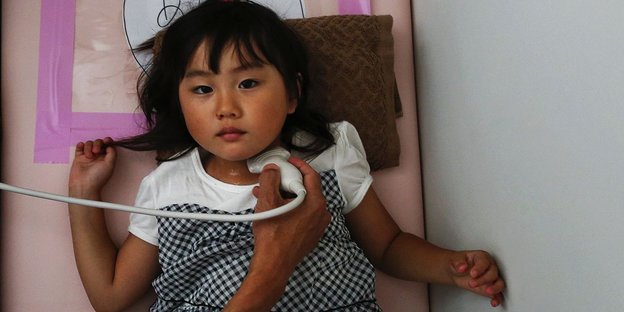 Ein kleines japanisches Mädchen liegt auf einer Liege und wird am Kehlkopf untersucht