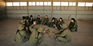 Soldatinnen sitzen in einem kahlen Gebäude audf dem Boden im Kreis