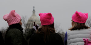 Drei Frauen mit rosa Mützen sitzen vor dem Kapitol in Washington