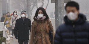 Viele chinesische Passanten laufen im nebliger Umgebung mit Atemschutzmasken