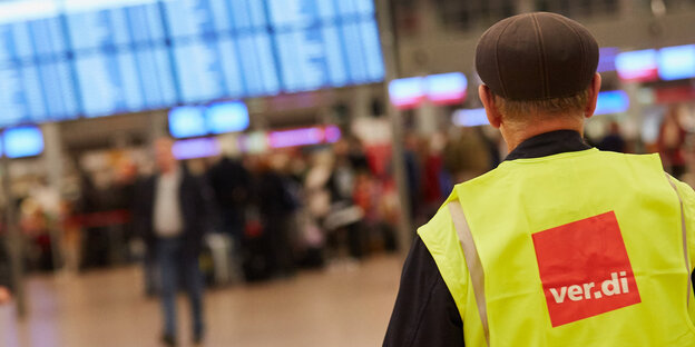 Ein Angestellter mit Verdi-Streikweste steht in einer Flughafenhalle