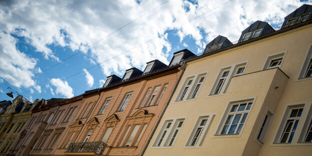 Eine Häuserreihe, die schief zur Seite gekippt erscheint, dahinter blau-weißer Himmel