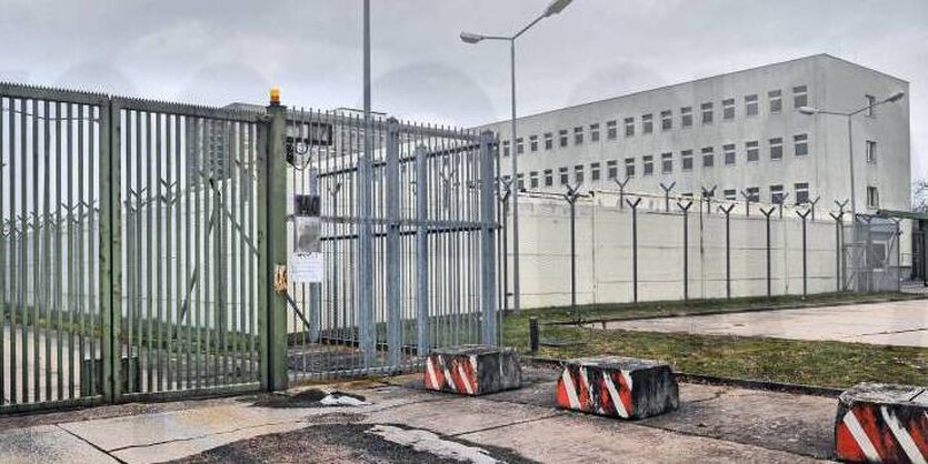 Hinter einem Zaun liegt ein graues Gebäude