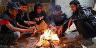 Afghanische Flüchtlinge sitzen frierend um ein Feuer in einer Belgrader Lagerhalle