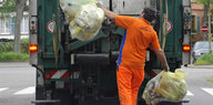 Ein Müllmann wirft zwei Plastiksäcke in den Müllabfuhrwagen