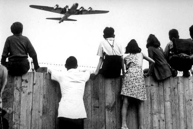 Kinder sitzen 1948 auf dem Zaun des Flughafens Tempelhof, während ein Rosinenbomber der US-Luftstreitkräfte zur Landung ansetzt