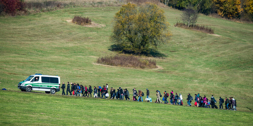 Menschen gehen in langer Schlange hinter einem Polizeifahrzeug her